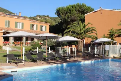 a pool with chairs and umbrellas next to a building at Hôtel Les Lentisques in Cargèse
