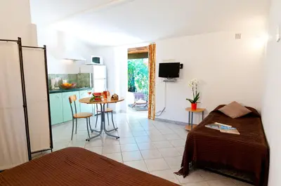a room with a bed and a kitchen with a table at Résidence Les Lièges de Palombaggia in Porto-Vecchio