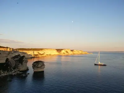 a sailboat in the water next to a cliff at chez dume in Bonifacio