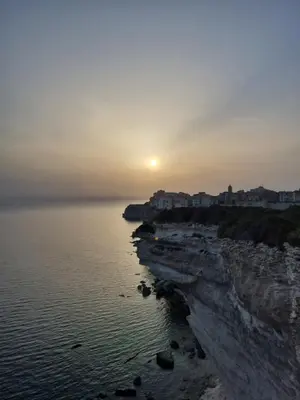a sunset over the ocean with houses on the shore at chez dume in Bonifacio