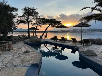 a swimming pool with chairs and umbrellas at sunset at Maranatha, front de mer avec plage in Porto-Vecchio