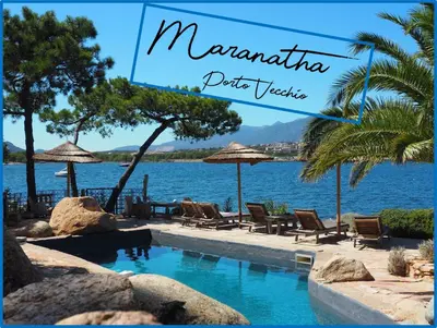 a garden with chairs and an umbrella next to the water at Maranatha, front de mer avec plage in Porto-Vecchio