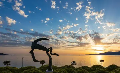 a statue in front of a body of water with the sunset at Radisson Blu Resort & Spa, Ajaccio Bay in Porticcio