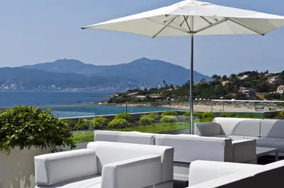 a patio with white chairs and an umbrella at Radisson Blu Resort & Spa, Ajaccio Bay in Porticcio