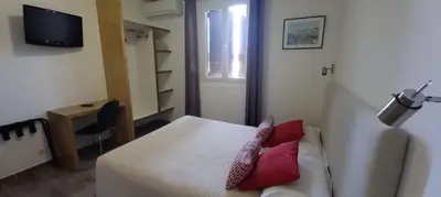 a room with a bed and a desk and a television at Hôtel du Golfe in Bonifacio