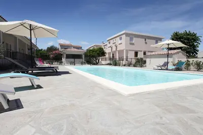a swimming pool with chairs and umbrellas next to a building at Hôtel Des Nacres in Ventiseri
