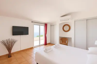 a white bedroom with a bed and a tv at La Veglia in Porto-Vecchio
