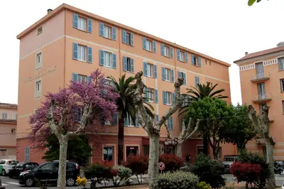 a large building with trees in front of it at Hotel de La Paix in Corte
