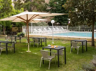 a group of tables and chairs with an umbrella next to a pool at Appart Hotel Corte HR in Corte