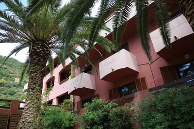 a pink building with a palm tree in front of it at Hotel Corsica - Porto Corse in Porto Ota