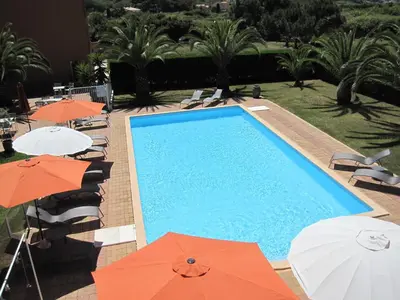 a swimming pool with orange and white umbrellas at Residence les Bell'ombres in Cargèse