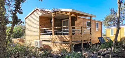 a tiny house with a porch and chairs in a yard at Camping Kévano Plage in Pianottoli-Caldarello