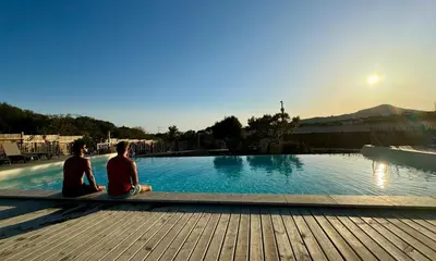 two men sitting next to a swimming pool at Camping Kévano Plage in Pianottoli-Caldarello