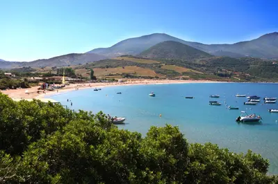 a beach with boats in the water and mountains at Camping du Soleil in Appietto