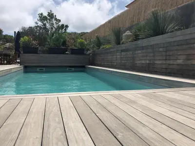 a swimming pool with a wooden floor and a retaining wall at Villa Orethaga Piscine 10 pers porto Vecchio in Porto-Vecchio