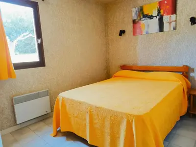 a bedroom with a bed with an orange bedspread and a window at Residence Maïna in Cargèse