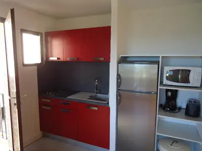 a kitchen with red cabinets and a stainless steel refrigerator at Residence Maïna in Cargèse
