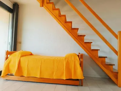 a bed with a yellow blanket sitting under a staircase at Residence Maïna in Cargèse