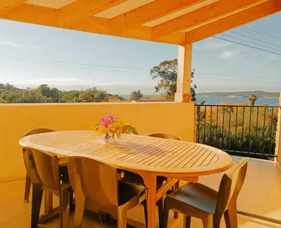 a wooden table and chairs on a patio with a view at Residence Maïna in Cargèse