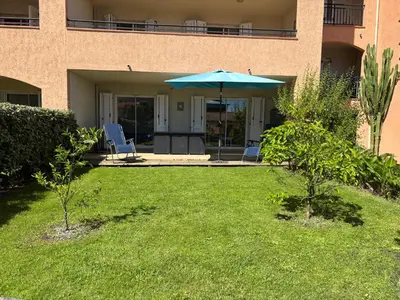 a patio with an umbrella and chairs in a yard at PALMERAIE 220 in Sari Solenzara