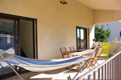a hammock on a balcony with a table and chairs at FILETTA in Sari Solenzara