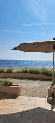 an umbrella sitting on a sidewalk near the ocean at Résidence Pascal Paoli Fior di Mare in Moriani Plage