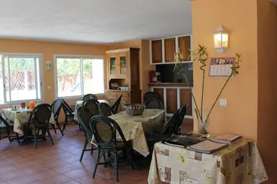 a dining room with tables and chairs and a kitchen at Chambres d'hôtes Le Clos des Oliviers in Sorbo-Ocagnano