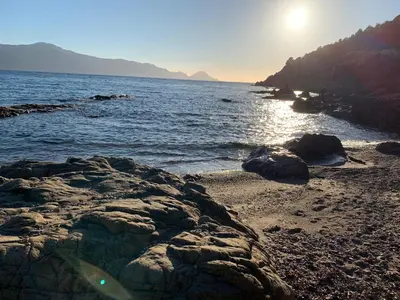 a beach with rocks and the sun rising over the water at Les Asphodèles in Partinello