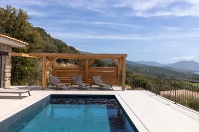 a swimming pool with two chairs on a patio with mountains in the background at Résidence La Plage in Propriano