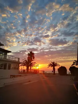 a sunset on the beach with palm trees and a building at Hotel & Restaurant San Pellegrino in Folelli