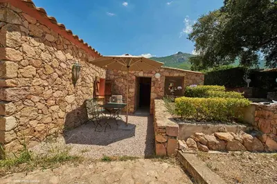 a stone building with a table and an umbrella at Maison L'Olivier avec piscine in Cuttoli-Corticchiato