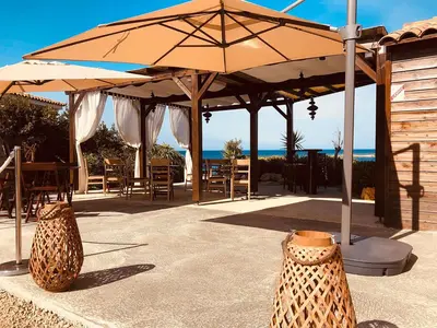 a patio with an umbrella and tables and chairs at Hôtel du Golfe in Sartène