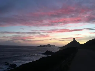 a sunset over the ocean with a lighthouse on a hill at VIzzavona piscine et jacuzzi in Ajaccio