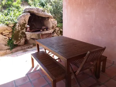 a wooden table and a bench next to a stone oven at Casa Myrta 3 étoiles in Porto-Vecchio