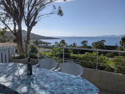 a table with white chairs and a bottle of wine on it at Appartements L'Acacia - plage d'Argent à 300m in Coti-Chiavari