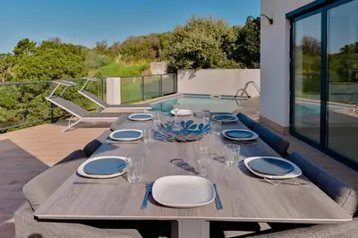 a wooden table with plates and wine glasses on a patio at Villa à l'entrée de Porticcio - Piscine - Vue dégagée in Cauro