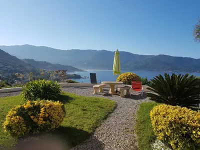 a patio with a table and a umbrella and flowers at Résidence U MELU GRAND T3 ROUGE en rez de jardin in Tiuccia