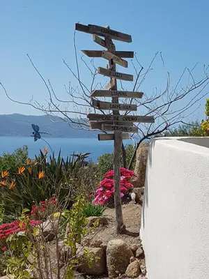 a wooden directional sign in a garden with flowers at Résidence U MELU Grand T2 BLEU en rez de jardin in Tiuccia