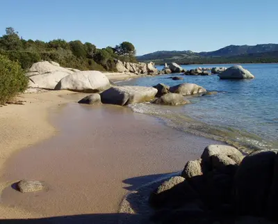 a group of rocks on a beach with water at La Baraka in Pianottoli-Caldarello