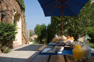 a wooden table with a blue umbrella and food on it at A l'ombre du clocher in Calenzana