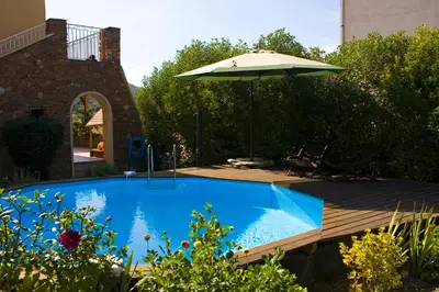 a swimming pool with an umbrella and a wooden deck at A l'ombre du clocher in Calenzana
