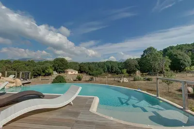 a large swimming pool with a wooden deck next to a field at Les Hauts de Cavanello in Zonza