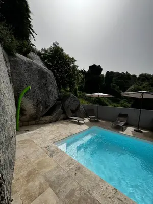 a swimming pool with two chairs and two umbrellas at Hotel Clair de Lune in Zonza