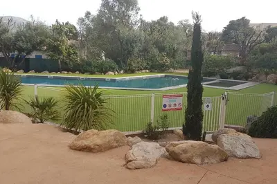 a fence in front of a swimming pool with rocks at APPARTEMENT TERRASSE CITA DI SALI PORTO VECCHIO in Porto-Vecchio