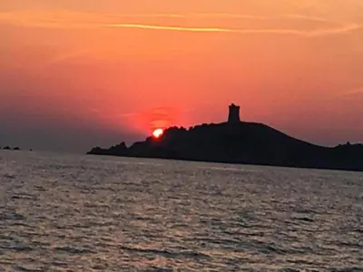 a sunset with a lighthouse on an island in the ocean at Romantic Retreat in Cargèse in Cargèse