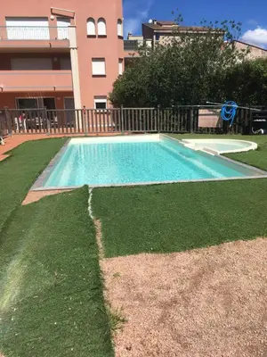 an empty swimming pool with grass and a building at Les princes du golf Jerome numero 13 quartier pascal paoli Appartement in Porto-Vecchio