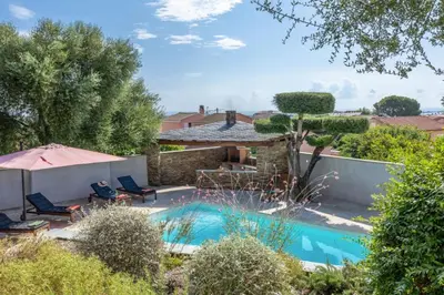 a swimming pool in a yard with two chairs and an umbrella at Villa Le Corps de Garde in Furiani