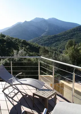 a chair and a table on a balcony with mountains at L'oliveraie du Fango in Manso