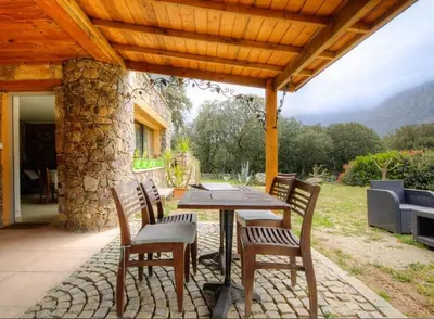 a patio with a table and chairs under a wooden roof at Appartement confortable à Moltifao, vue sur montagne, 50 m² in Moltifao