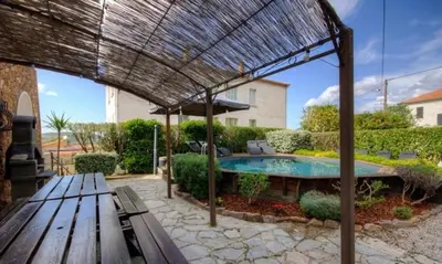 a patio with a bench and an umbrella and a pool at Gîte A l'ombre du clocher in Calenzana